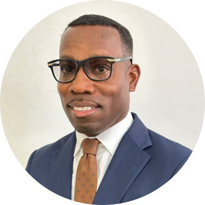 Man in a suit and tie wearing glasses, standing against a plain white background.