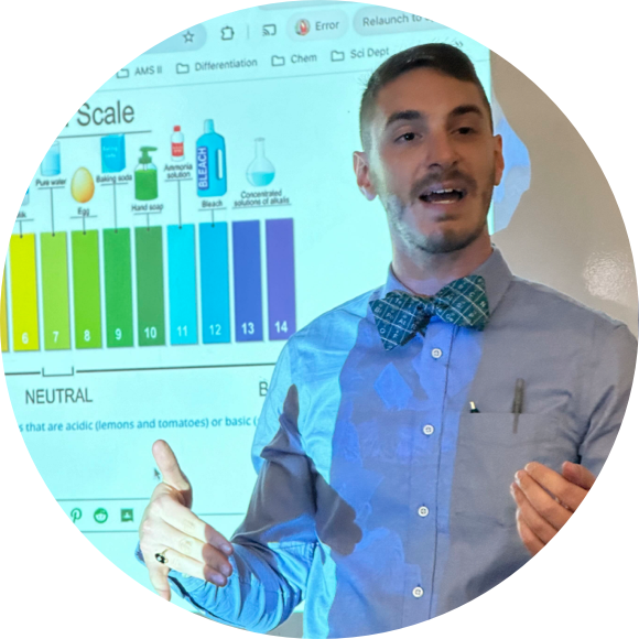 A person is speaking in front of a projected image showing a pH scale diagram. They are wearing a shirt, bow tie, and have a pen clipped to their pocket.