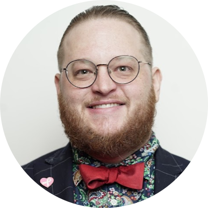 A person with glasses and a beard, wearing a red bow tie, a dark jacket with pinstripes, and a colorful, patterned shirt.