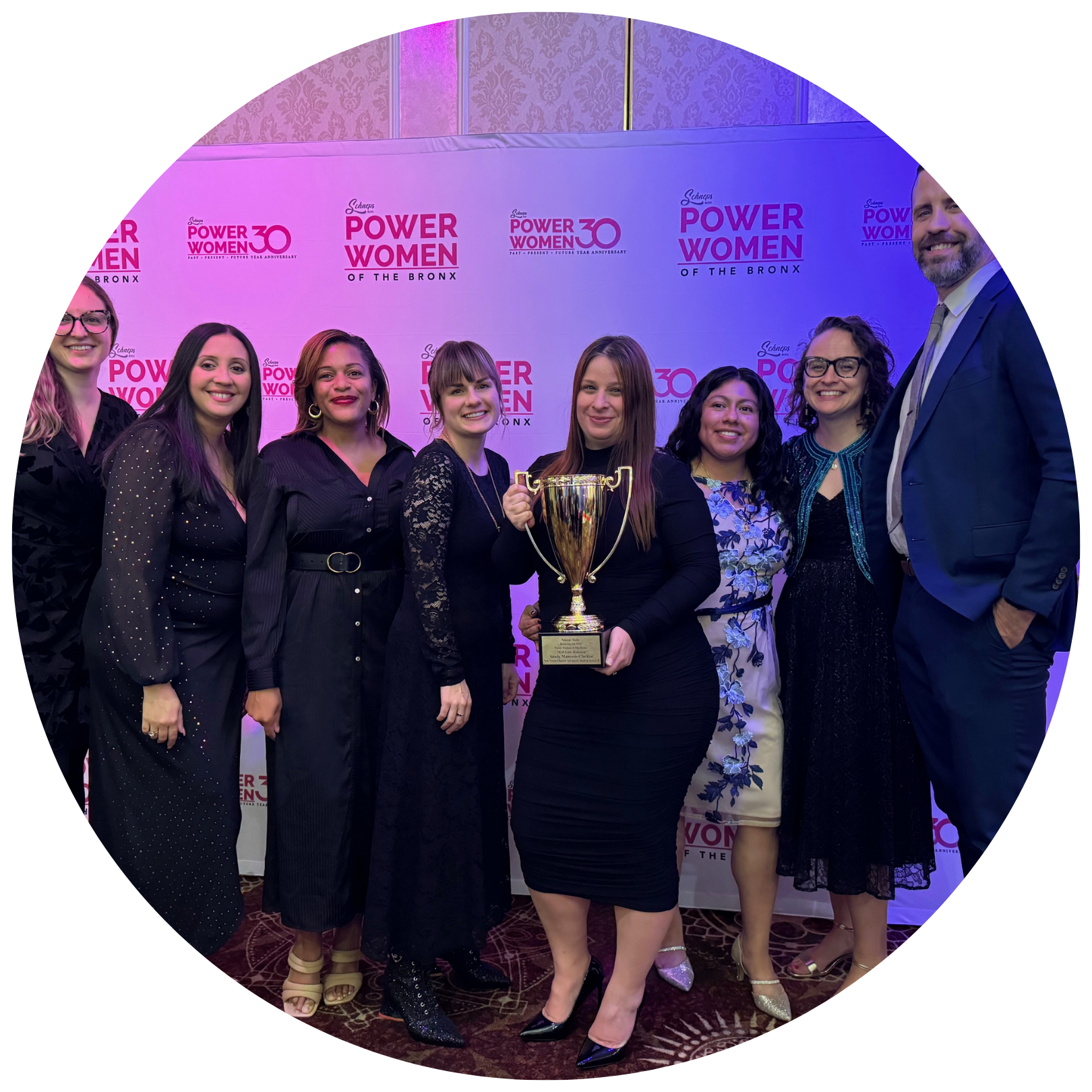 A group of people stands together, with one person holding a trophy, in front of a banner reading "Power Women of the Bronx.