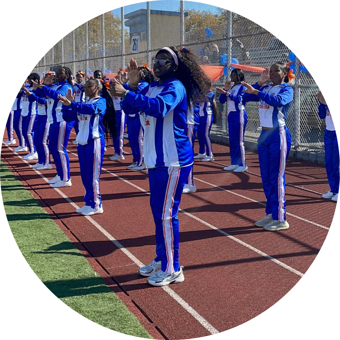 Cheerleaders in blue and white uniforms perform a routine on a track field, clapping in unison.