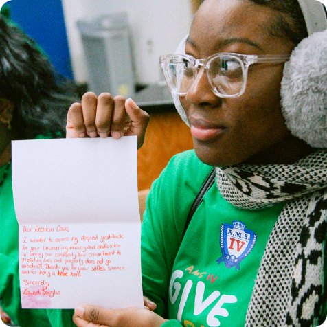 A person wearing earmuffs, glasses, and a green shirt holds an open handwritten card with a message of gratitude.